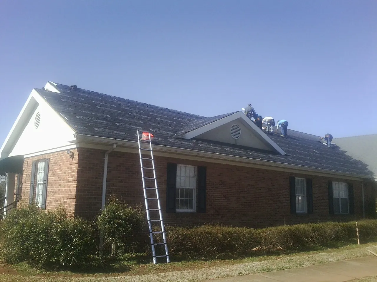 Crew tearing shingles off a brick ranch roof with a ladder set — Emergency Roof Repair work by our crew in Michigantown