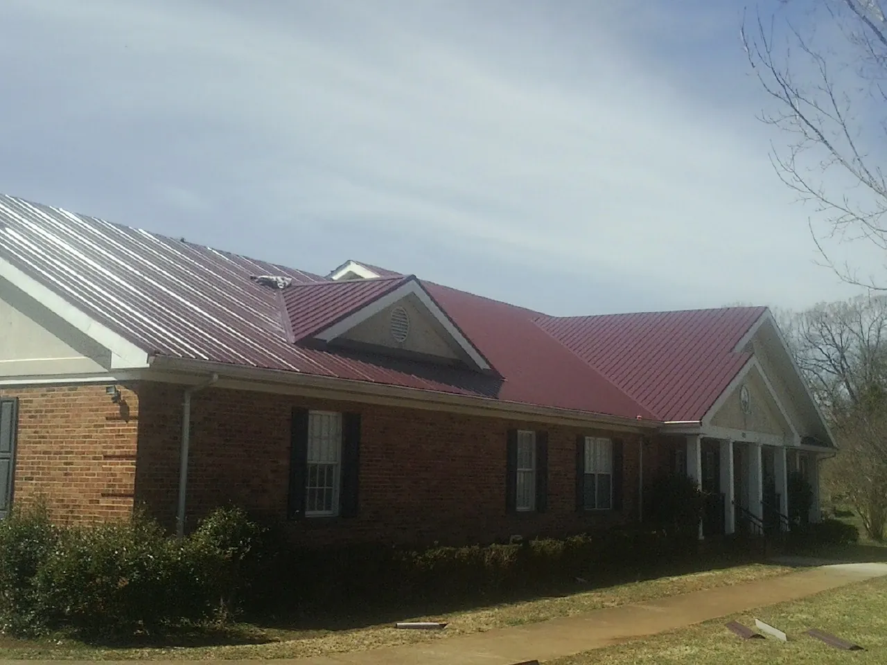 Red metal roof with gabled entries on a long brick building, from a Hail Damage Roof Repair job in Michigantown