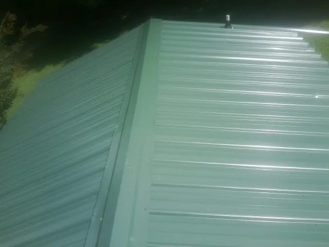 New green metal panels meeting at the ridge of a roof — Flat Roof Repair work by our crew in Michigantown