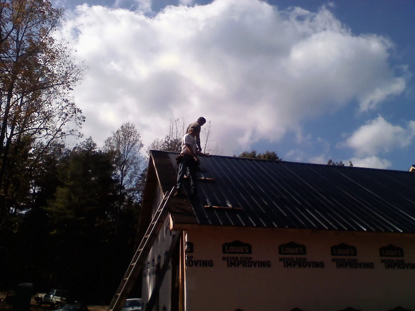 Roofer fastening dark metal panels high against a cloudy sky, from a Roof Inspection job in Michigantown