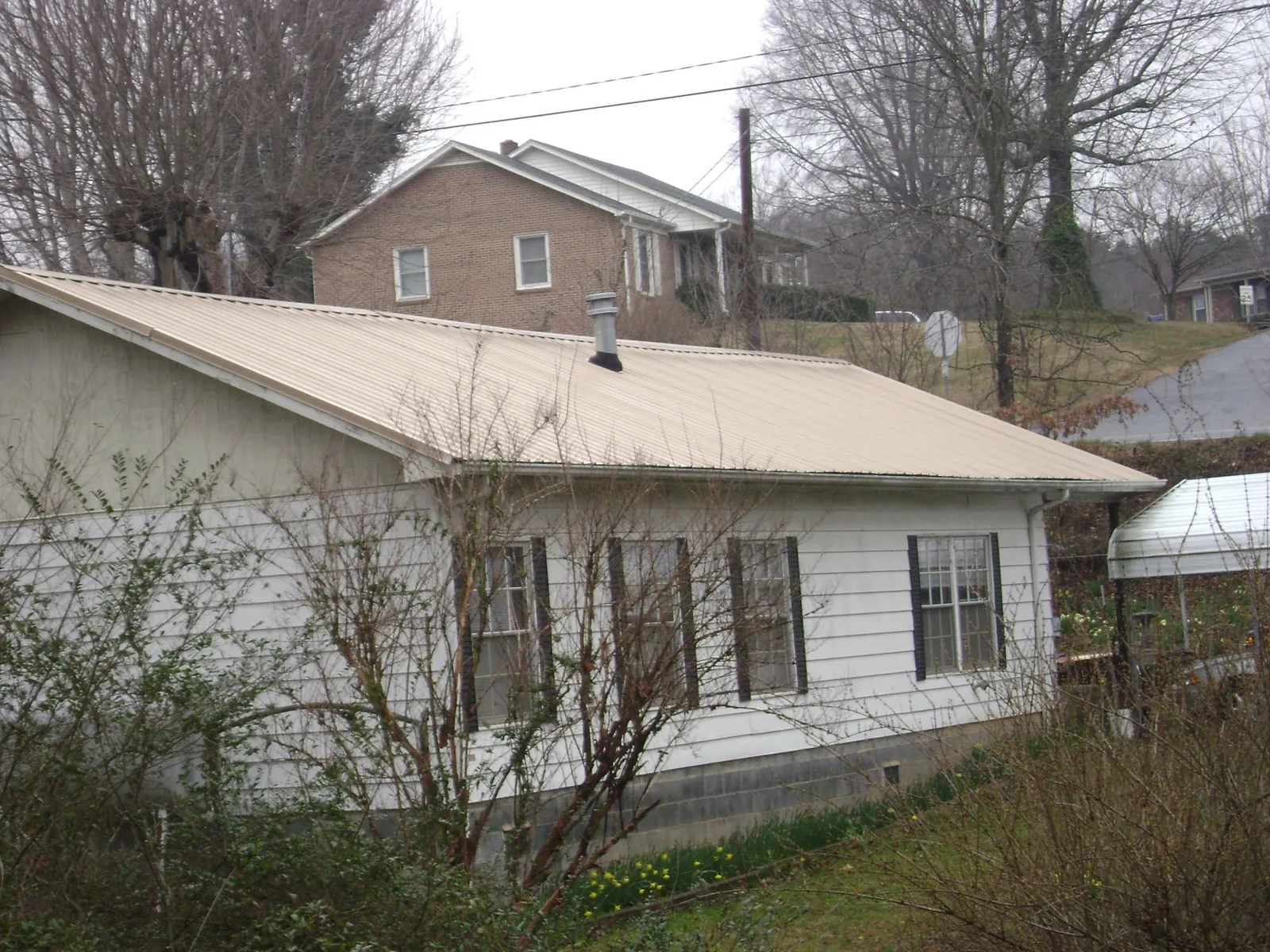 Tan metal roof on a white sided house set into a hillside — Commercial Roofing by Roofing Brothers in Michigantown