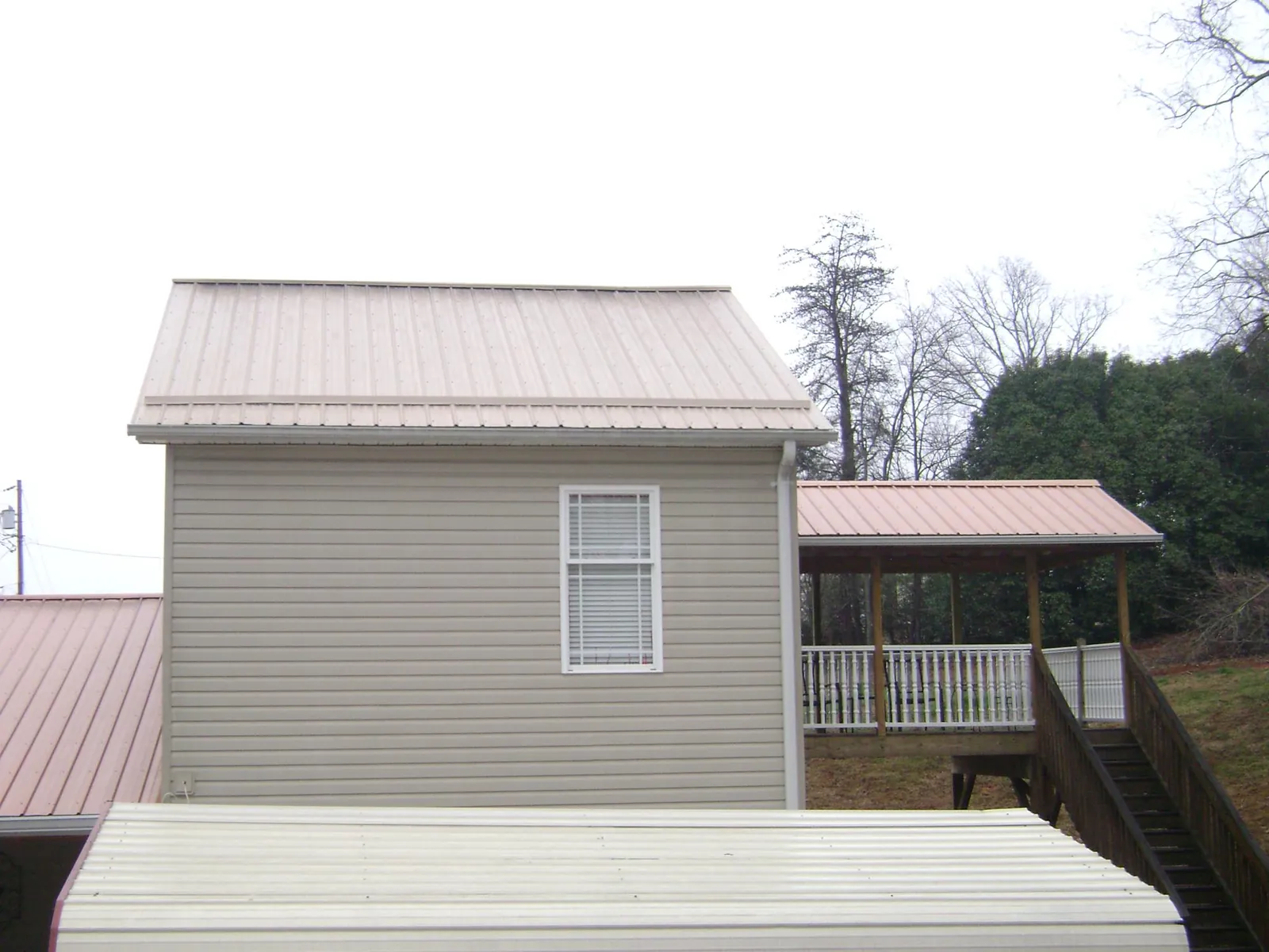 Tan metal roofs on a two story addition and attached porch, from a Roof Replacement job in Michigantown